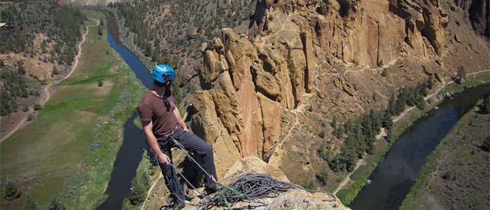 Photo of a rock climber on top of a cliff looking down at the valley and river below