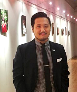 Portrait of Liam Ward standing in a gallery in front of his artwork