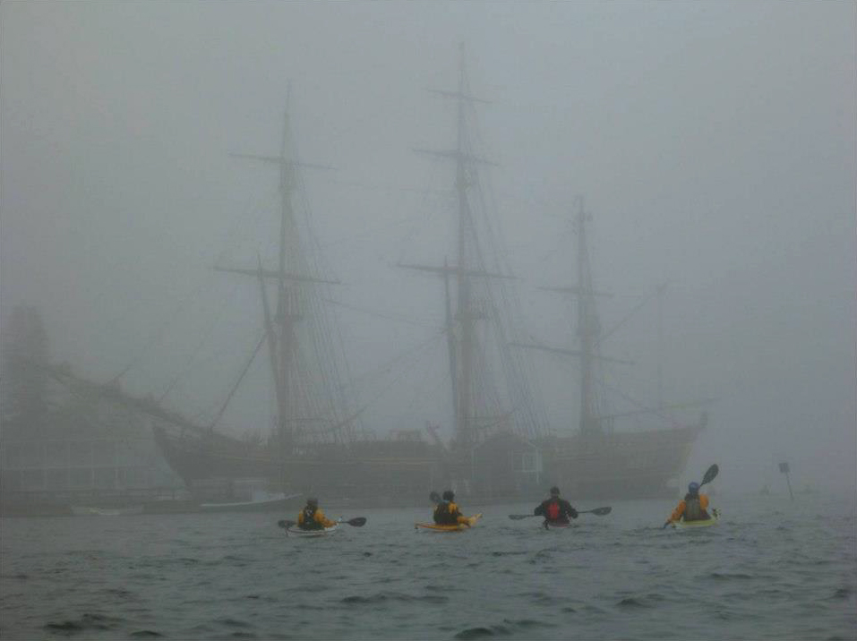 Students kayak past a tall-mast sailing ship