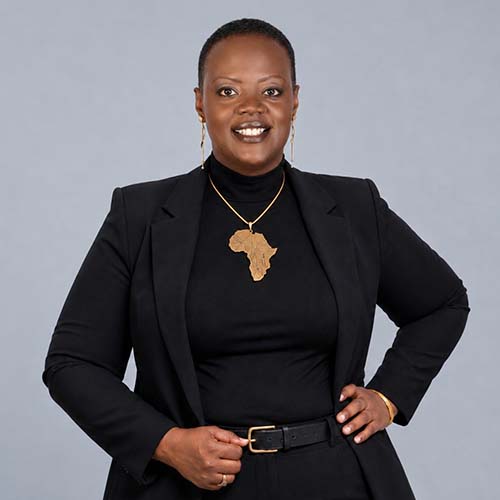 Woman with short black hair wearing a black pantsuit stands for a photo. She wears a necklace with the continent of Africa.