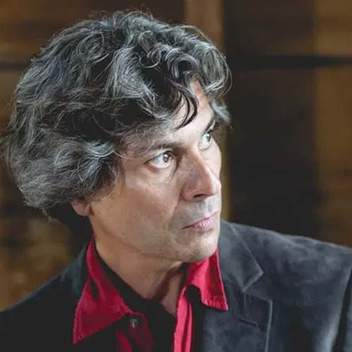 A dramatic headshot of a man with wavy salt and pepper hair, a downward-facing side profile angle.