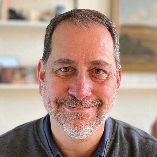 Man with grey Henley shirt in office smiles.