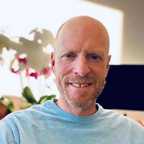 Man in a sunny room wearing a blue t-shirt smiles for the camera