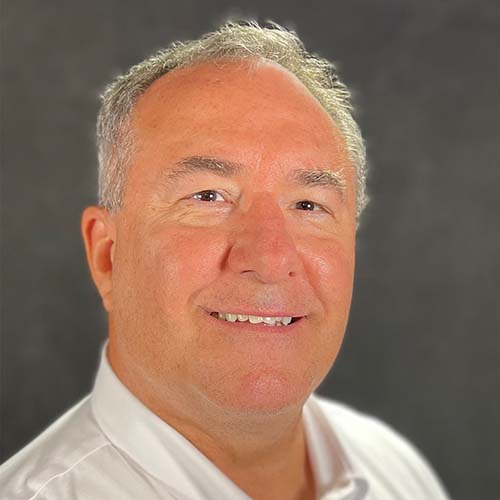 Man with white shirt and white gray hair smiles for the camera in a headshot against a gray background.