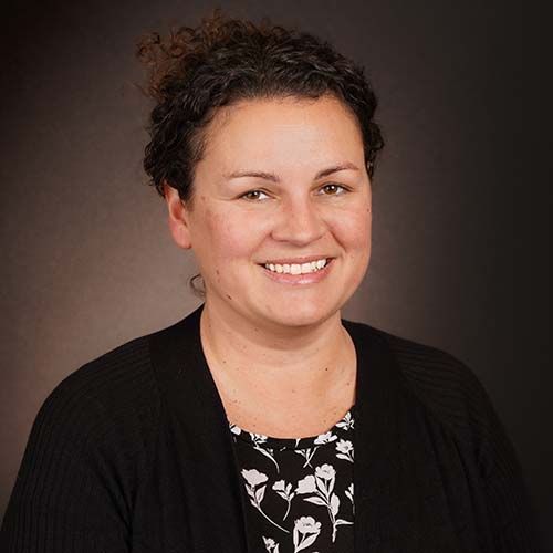 Professional photo of woman, curly hair pulled back away from her face. She smiles brightly.