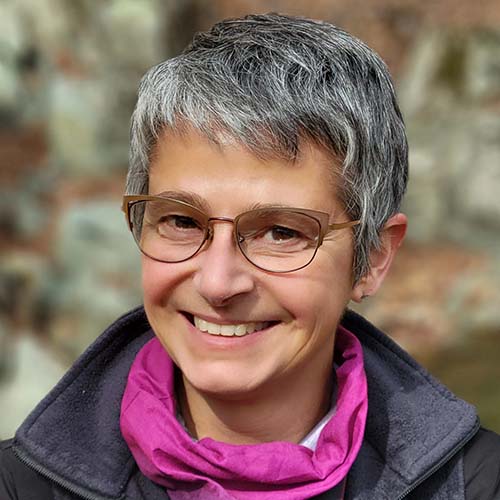 Woman with a salt-and-pepper colored pixie-cut wearing glasses, outside in hiking gear