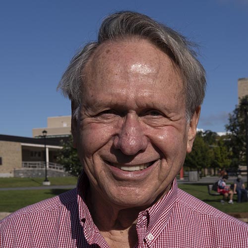 Man with a gray hair and red and white plaid shirt standing outside with bright blue sky in the background