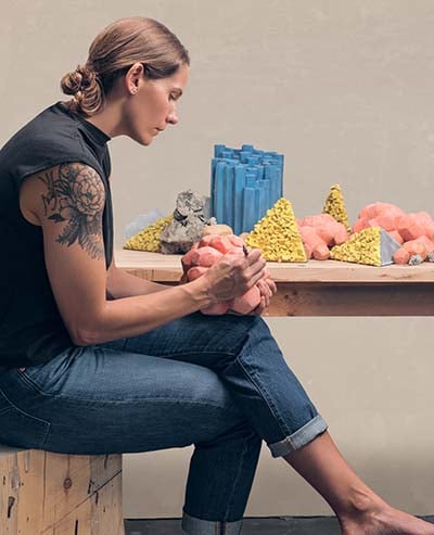 woman sits on a tree trunk stool working with clay