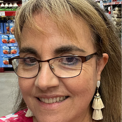 Close-up headshot of a woman with dark rimmed metal glasses and dangly earrings.