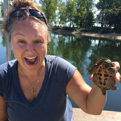 Danielle Garneau holding up a musk turtle on the bank of Lake Champlain