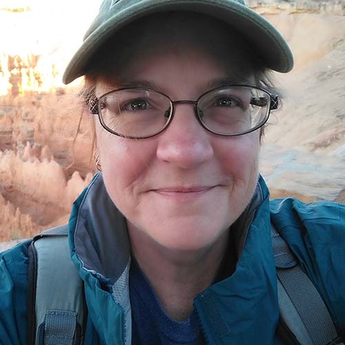 close-up shot of woman out hiking, wearing baseball cap and smiling close-mouthed at the camera