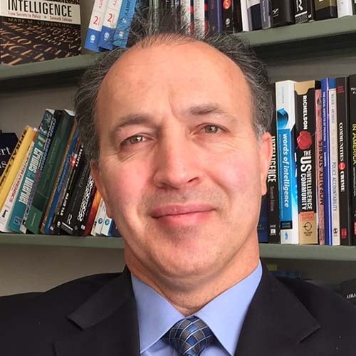 Man in a dark suit in front of a book shelf.