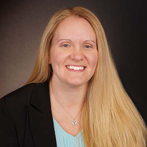 Woman with a black blazer and teal shirt and long blond hair sits for a professional headshot