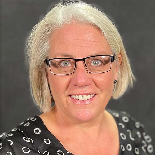 Woman with chin-length white hair and dark-rimmed glasses smiles brightly for the camera