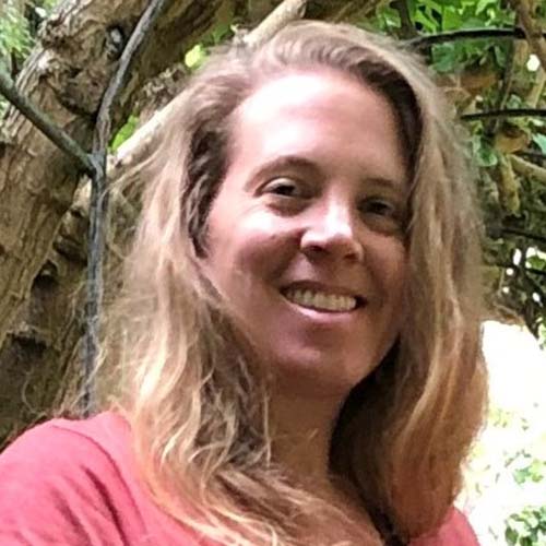 Woman with long blond hair in a tropical setting smiles for the camera