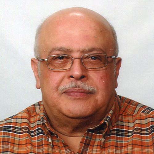 Man with white mustache and orange and blue plaid shirt smiles slightly for the camera.