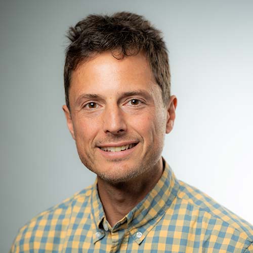 Man wearing a yellow and blue plaid button up sits for a professional headshot.