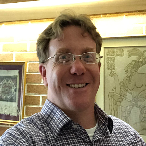 Dr. Justin Lowry stands in front of framed art in a brick-lined hallway