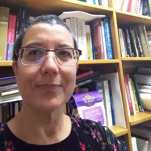 Woman with her dark hair pulled back standing in front of a bookshelf.