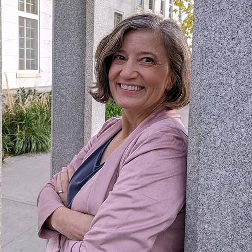 Michelle Ouellette wearing a pink blazer and leans up against a marble post.