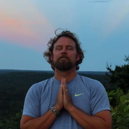 A man at twilight stands with eyes closed, head back and hands in a grateful gesture.