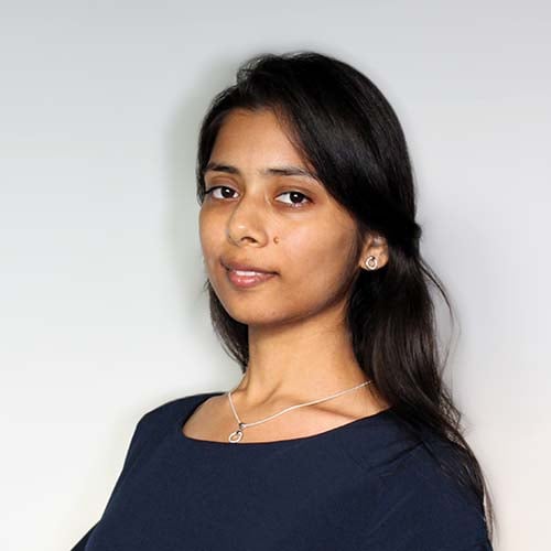 Woman standing against a white wall, wearing a dark blue flowy shirt, head and body turned slightly sideways.