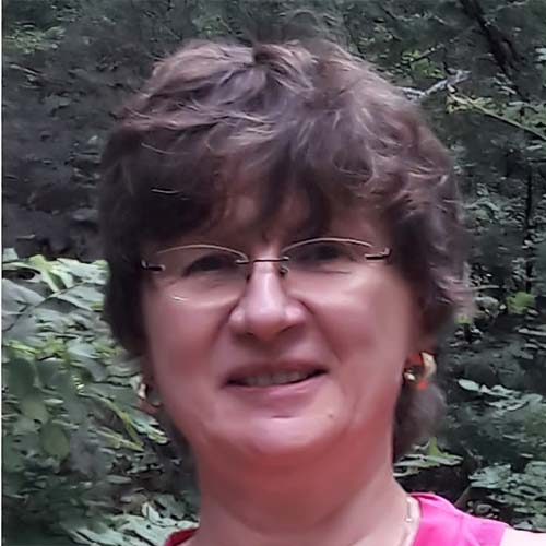Woman standing outside against some greenery, wearing a pink shirt.