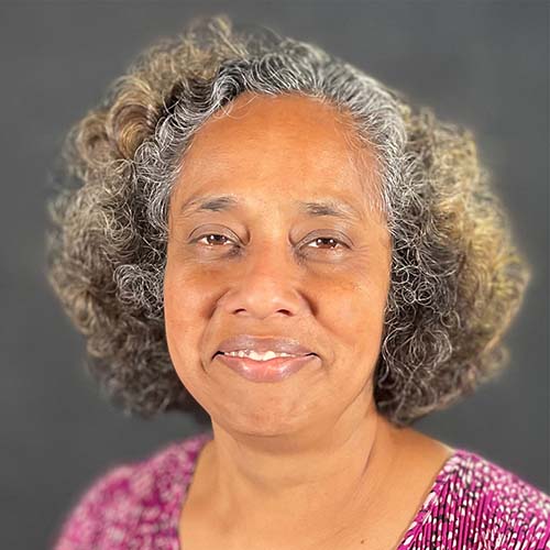 Woman with curly dark and graying hair smiles for the camera against a dark gray background