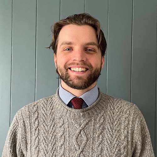 Man smiles brightly for headshot while standing in front of a paneled wall background.