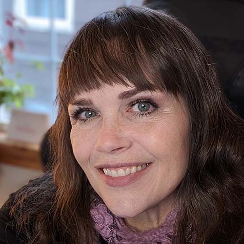 A woman with auburn hair wearing a knitted scarf around her neck smiles for a the camera
