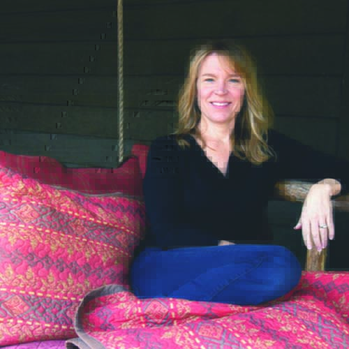 Woman sitting with legs up on a daybed, located on an outside porch.