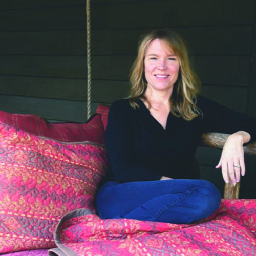 Woman sitting with legs up on a daybed, located on an outside porch.