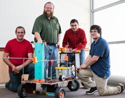Dr. Mike Walters poses with students in the robotics club and a robot they built