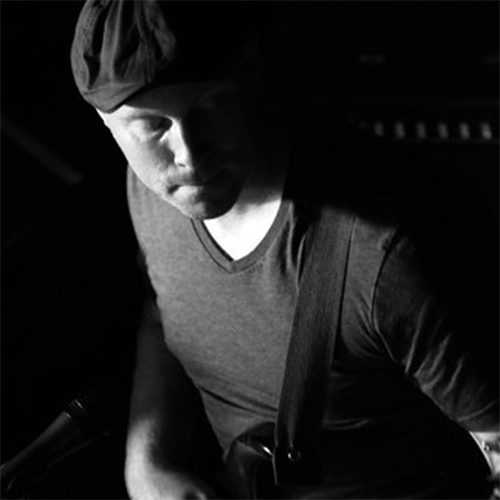 Black and white image of J. Ward playing guitar, shot from above