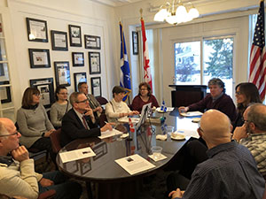 Scholars and leaders sit around an oval table. The American, Canadian and Quebec flags are visible.