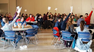 Photo of students raising their hands hoping to be called on during a round of math jeopardy