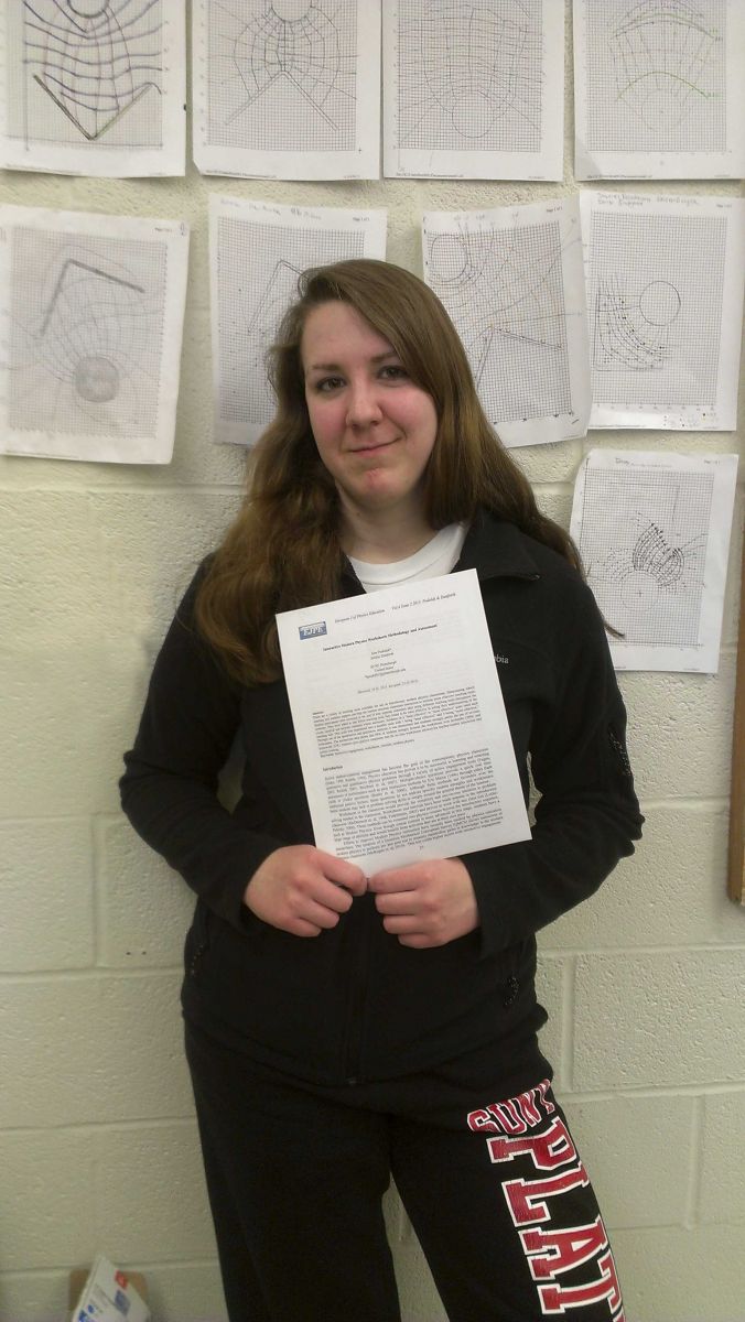 Jordyn is holding her paper, and standing in front of a wall display of similar papers