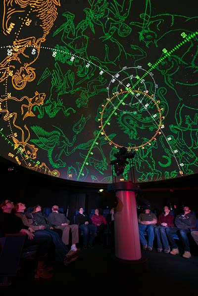 Photo of people watching a show that features a projection of constellations on the planetarium dome