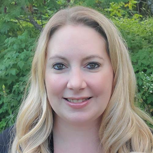 woman with long blond wavy hair stands outside smiling for the camera