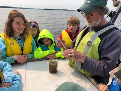 Young students on a boat on the lake learn how to do a water quality test