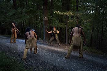 Photograph of a man on a dirt road in the woods in a defensive stance, surrounded by 3 Native Americans. A sign reads "No Trespassing"