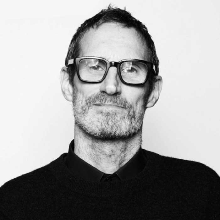 Black and white portrait of Michael Jager with a bemused expression on his face while wearing glasses and a dark shirt
