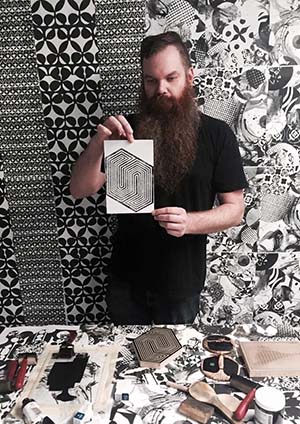 The artist holds a woodblock print surrounded by geographic black and white prints
