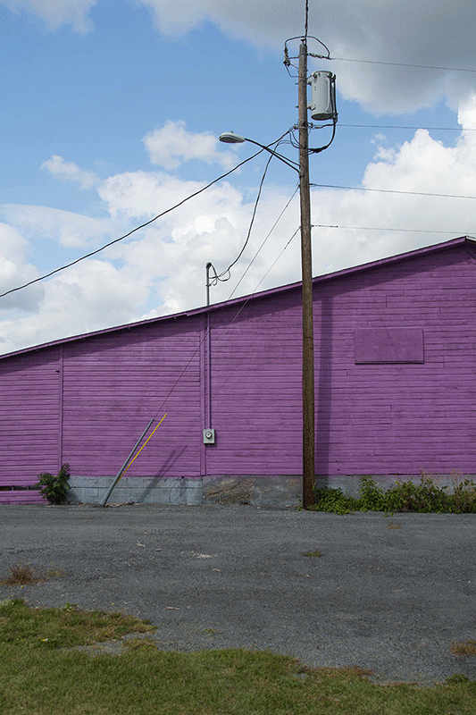 Photograph of a purple wall with a utility pole next to it. The wall has a gentle slope.