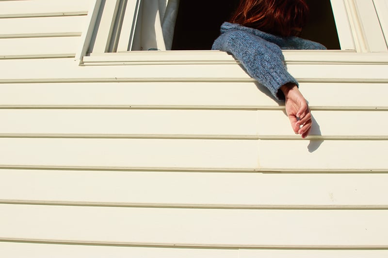 Photo of a person hanging their arm outside a white paneled house.